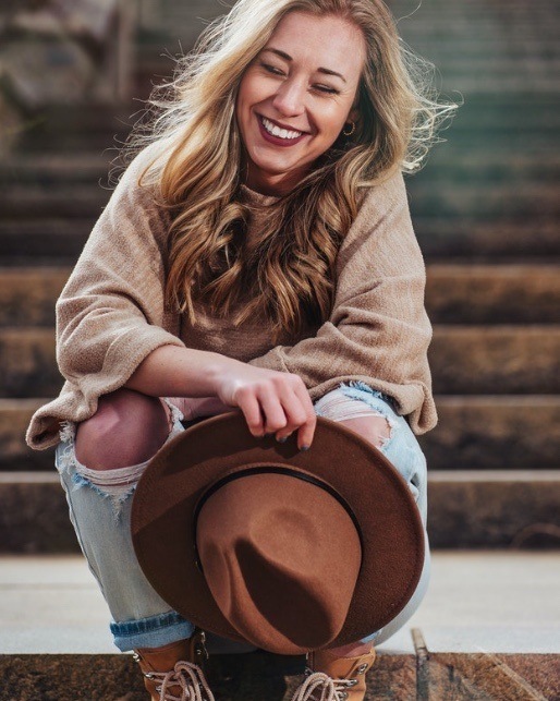 woman sitting outside smiling with eyes closed holding hat 