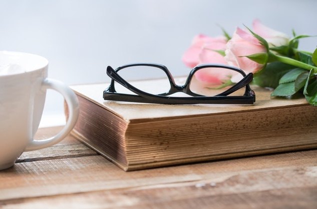 pink roses and black rimmed glasses on top of with coffee mug