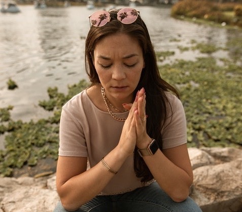 woman with sunglasses on head with hand pressed together sitting near ake