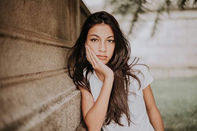 woman with leaning against a wall with hand against face