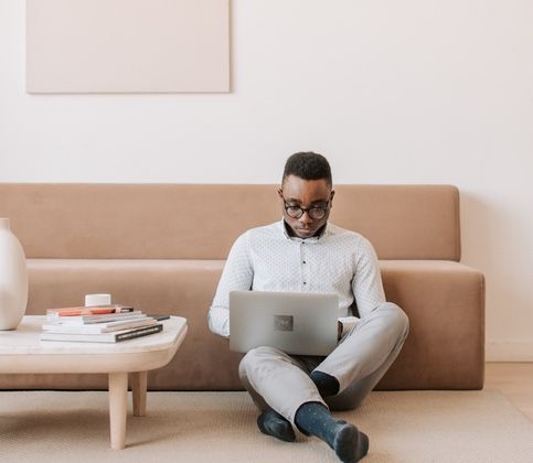man sitting against couch with laptop in lap next to coffee table 